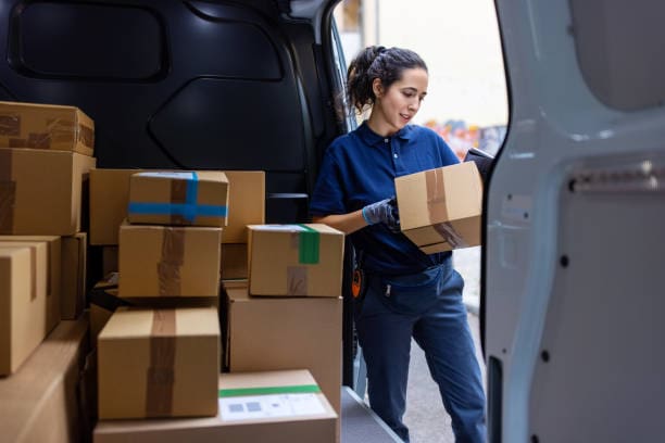Female courier standing by shipping van checking the parcel for delivery. Woman looking at the delivery address of the parcel in van.